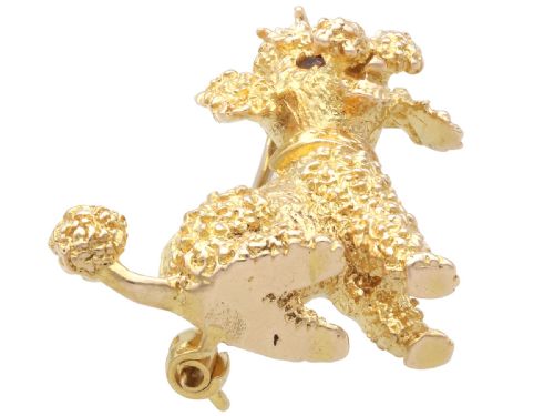 fig 5. A 9ct yellow gold brooch sculpted as a seated poodle with textured fur and red garnet eyes holding a stick in its mouth.