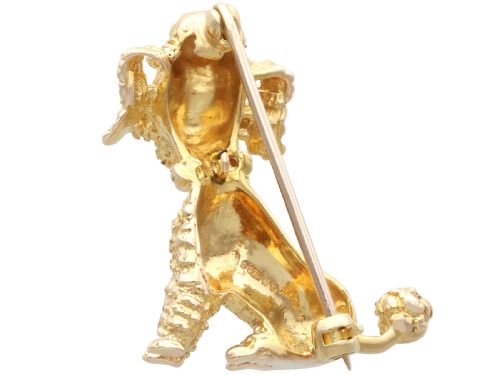 fig 6. A 9ct yellow gold brooch sculpted as a seated poodle with textured fur and red garnet eyes holding a stick in its mouth.