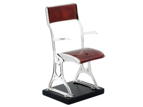 fig 4. A miniature sterling silver folding chair with brown enamel seat and backrest panels mounted on a black rectangular base.