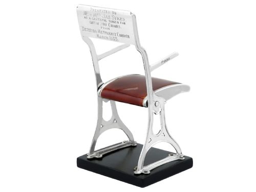 fig 5. A miniature sterling silver folding chair with brown enamel seat and backrest panels mounted on a black rectangular base.