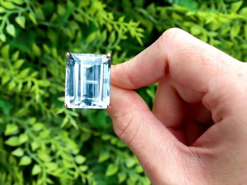 fig 1. A substantial rectangular emerald-cut light blue aquamarine gemstone secured in a four-claw 18ct yellow gold ring mounting.