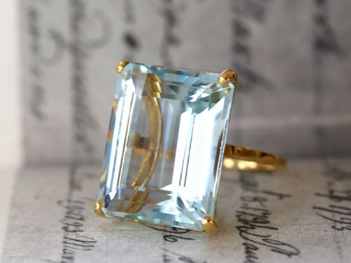 fig 2. A substantial rectangular emerald-cut light blue aquamarine gemstone secured in a four-claw 18ct yellow gold ring mounting.