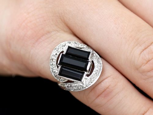 fig 2. An Art Deco style platinum dress ring displaying three vertical rectangular black onyx plaques enclosed within a circular diamond-set halo frame.