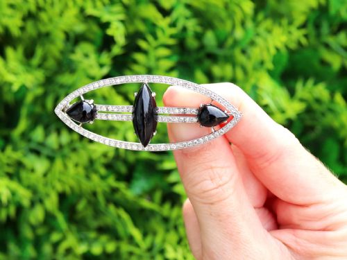 fig 1. An Art Deco platinum brooch featuring an openwork navette frame set with diamonds and three carved black onyx stones.