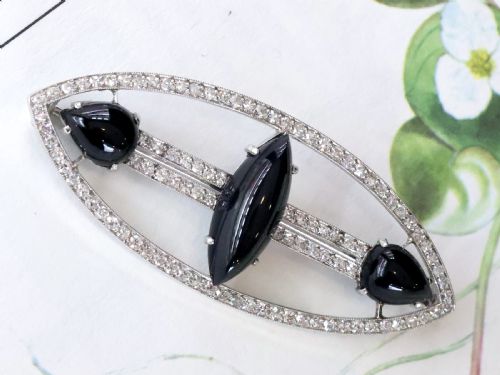 fig 2. An Art Deco platinum brooch featuring an openwork navette frame set with diamonds and three carved black onyx stones.
