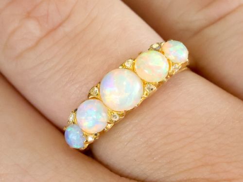 fig 2. An Edwardian 18ct yellow gold five stone ring featuring graduated cabochon white opals with small diamond accents and full interior British hallmarks.