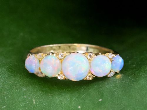 fig 5. An Edwardian 18ct yellow gold five stone ring featuring graduated cabochon white opals with small diamond accents and full interior British hallmarks.
