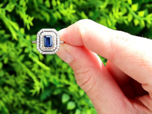 fig 1. An 18ct yellow gold ring featuring a central emerald-cut blue sapphire framed by a geometric double halo of round diamonds with millegrain edging.