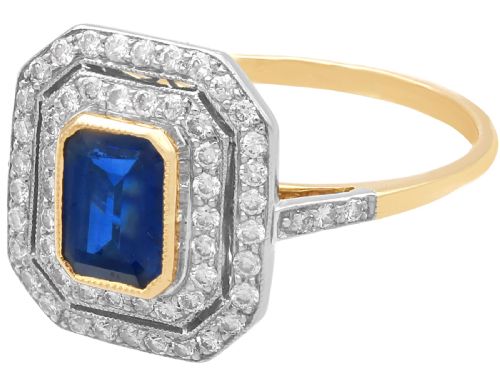 fig 5. An 18ct yellow gold ring featuring a central emerald-cut blue sapphire framed by a geometric double halo of round diamonds with millegrain edging.