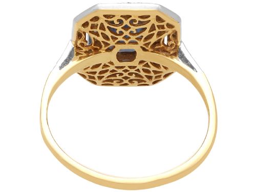 fig 6. An 18ct yellow gold ring featuring a central emerald-cut blue sapphire framed by a geometric double halo of round diamonds with millegrain edging.