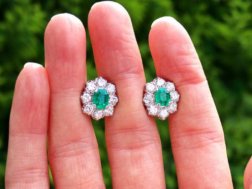 fig 1. A pair of 18ct white gold cluster earrings featuring central emerald-cut green emeralds surrounded by a halo of round brilliant diamonds.