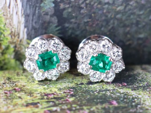 fig 2. A pair of 18ct white gold cluster earrings featuring central emerald-cut green emeralds surrounded by a halo of round brilliant diamonds.