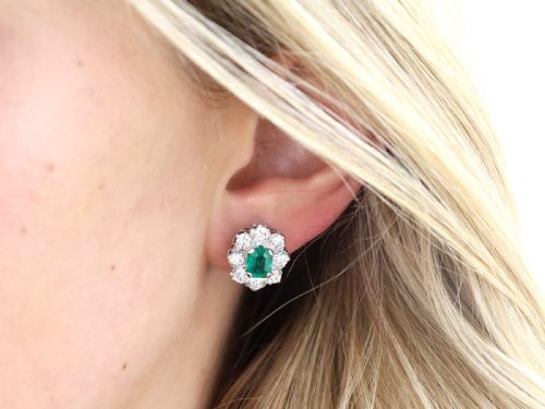 fig 3. A pair of 18ct white gold cluster earrings featuring central emerald-cut green emeralds surrounded by a halo of round brilliant diamonds.