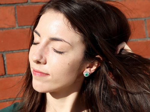 fig 8. A pair of 18ct white gold cluster earrings featuring central emerald-cut green emeralds surrounded by a halo of round brilliant diamonds.