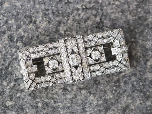 fig 2. A rectangular Art Deco platinum brooch featuring intricate geometric openwork millegrain setting filled with round diamonds surrounding a central bezel-set diamond.