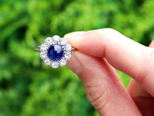 fig 1. A platinum ring set with a central round cabochon blue sapphire surrounded by a halo of ten round diamonds.