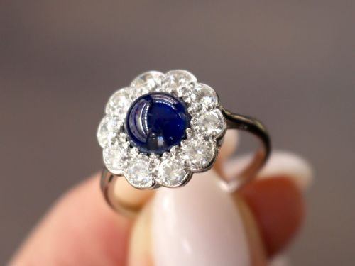 fig 2. A platinum ring set with a central round cabochon blue sapphire surrounded by a halo of ten round diamonds.