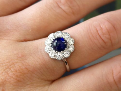 fig 3. A platinum ring set with a central round cabochon blue sapphire surrounded by a halo of ten round diamonds.