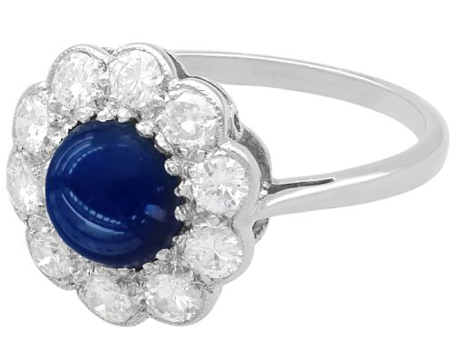 fig 5. A platinum ring set with a central round cabochon blue sapphire surrounded by a halo of ten round diamonds.
