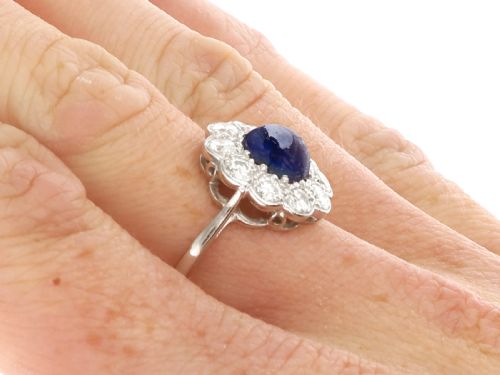 fig 9. A platinum ring set with a central round cabochon blue sapphire surrounded by a halo of ten round diamonds.