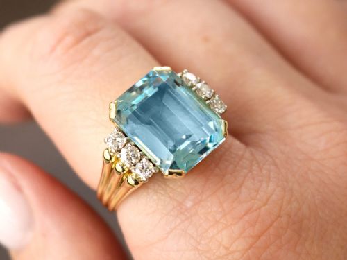 fig 3. A 14ct yellow gold dress ring featuring a large emerald-cut light blue aquamarine central gemstone flanked by six round diamonds.