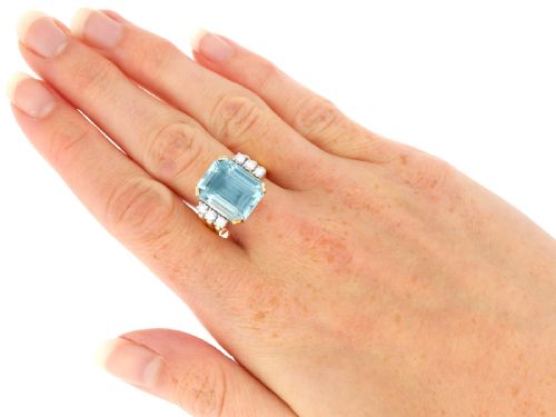 fig 9. A 14ct yellow gold dress ring featuring a large emerald-cut light blue aquamarine central gemstone flanked by six round diamonds.