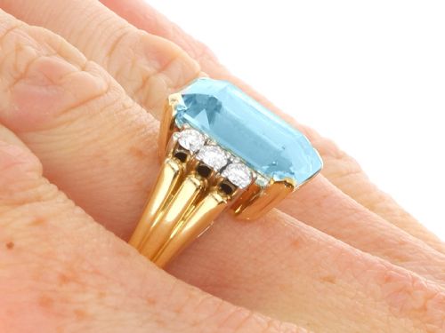 fig 10. A 14ct yellow gold dress ring featuring a large emerald-cut light blue aquamarine central gemstone flanked by six round diamonds.