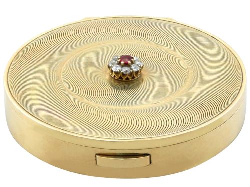 fig 7. A circular 9ct yellow gold powder compact featuring an engine-turned swirling pattern and a central ruby and diamond cluster.