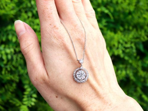 fig 1. An antique platinum halo pendant featuring a central round diamond surrounded by a scalloped border of smaller diamonds on a fine chain.