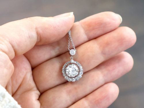 fig 2. An antique platinum halo pendant featuring a central round diamond surrounded by a scalloped border of smaller diamonds on a fine chain.