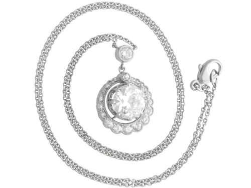 fig 6. An antique platinum halo pendant featuring a central round diamond surrounded by a scalloped border of smaller diamonds on a fine chain.