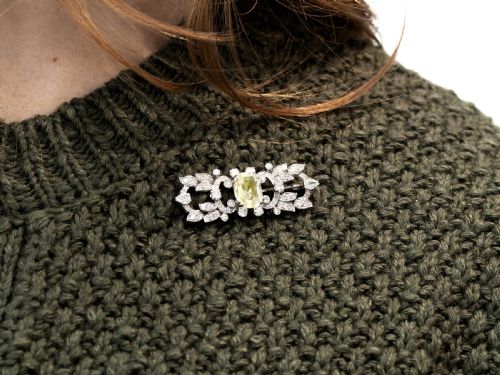fig 2. An Art Deco platinum brooch centered with an oval cushion-cut yellow sapphire enclosed by diamond-set scrollwork and foliate motifs.