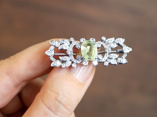 fig 3. An Art Deco platinum brooch centered with an oval cushion-cut yellow sapphire enclosed by diamond-set scrollwork and foliate motifs.