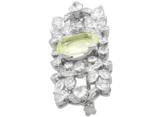 fig 5. An Art Deco platinum brooch centered with an oval cushion-cut yellow sapphire enclosed by diamond-set scrollwork and foliate motifs.