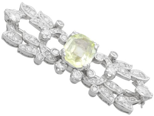fig 6. An Art Deco platinum brooch centered with an oval cushion-cut yellow sapphire enclosed by diamond-set scrollwork and foliate motifs.