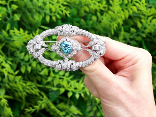 fig 1. An oval Art Deco platinum brooch featuring an openwork geometric frame set with diamonds and a central round brilliant blue zircon.