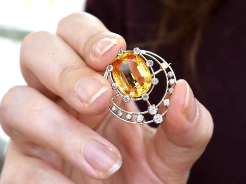 fig 2. A circular 14ct yellow gold openwork brooch featuring a central oval cut yellow topaz framed by diamond settings.