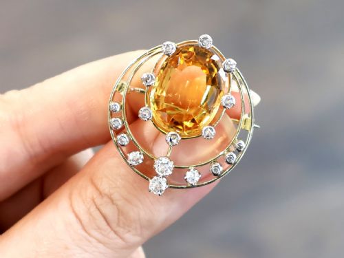 fig 3. A circular 14ct yellow gold openwork brooch featuring a central oval cut yellow topaz framed by diamond settings.
