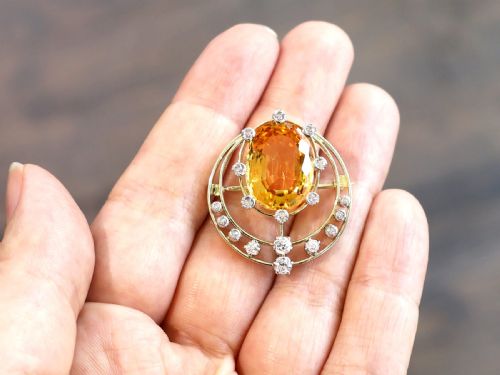 fig 4. A circular 14ct yellow gold openwork brooch featuring a central oval cut yellow topaz framed by diamond settings.
