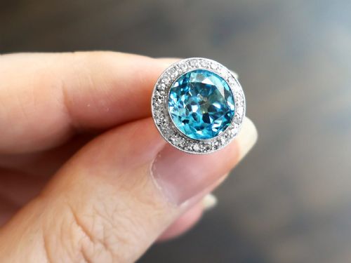 fig 2. A pair of 14ct white gold stud earrings featuring round blue zircon gemstones encircled by diamond halos with millegrain borders.
