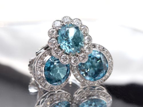 fig 4. A pair of 14ct white gold stud earrings featuring round blue zircon gemstones encircled by diamond halos with millegrain borders.