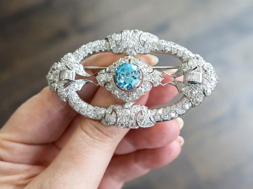 fig 2. An oval Art Deco platinum brooch featuring an openwork geometric frame set with diamonds and a central round brilliant blue zircon.