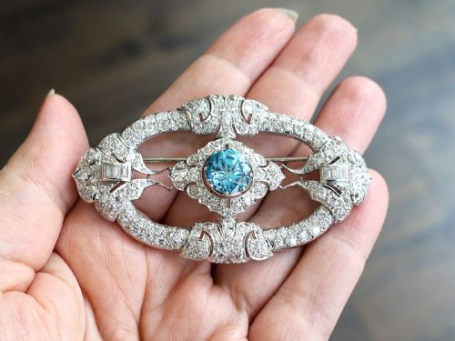 fig 3. An oval Art Deco platinum brooch featuring an openwork geometric frame set with diamonds and a central round brilliant blue zircon.