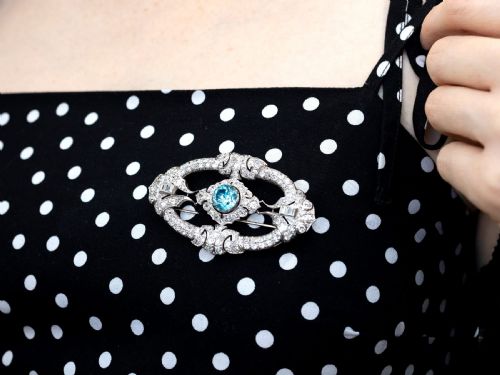 fig 4. An oval Art Deco platinum brooch featuring an openwork geometric frame set with diamonds and a central round brilliant blue zircon.