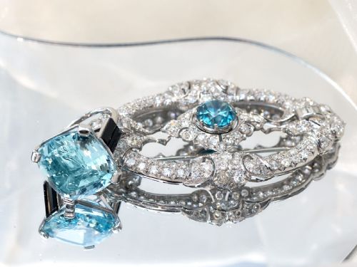 fig 5. An oval Art Deco platinum brooch featuring an openwork geometric frame set with diamonds and a central round brilliant blue zircon.