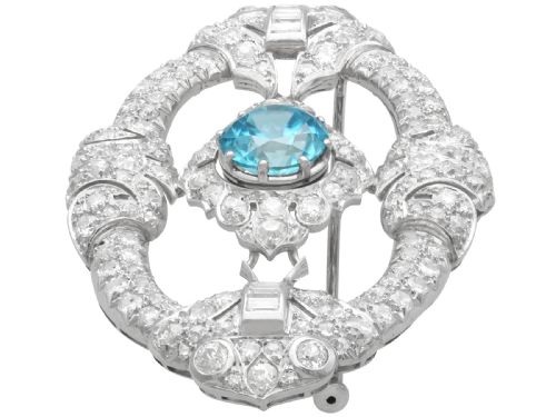 fig 6. An oval Art Deco platinum brooch featuring an openwork geometric frame set with diamonds and a central round brilliant blue zircon.