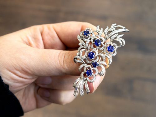 fig 2. An Art Deco platinum brooch styled as a floral spray, set with round blue sapphires and accented with pave and baguette-cut diamonds.