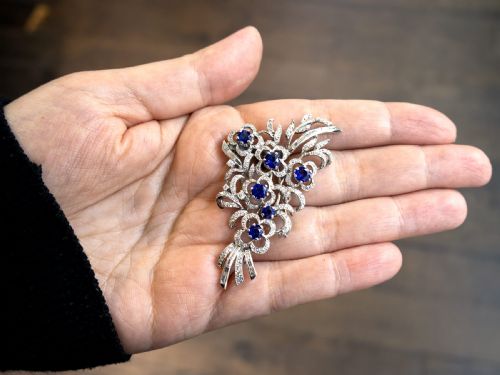 fig 3. An Art Deco platinum brooch styled as a floral spray, set with round blue sapphires and accented with pave and baguette-cut diamonds.