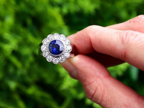 fig 1. A vintage 18ct white gold cluster ring set with a central round blue sapphire surrounded by a halo of brilliant diamonds with a scalloped edge.