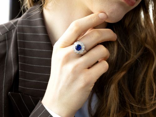 fig 5. A vintage 18ct white gold cluster ring set with a central round blue sapphire surrounded by a halo of brilliant diamonds with a scalloped edge.